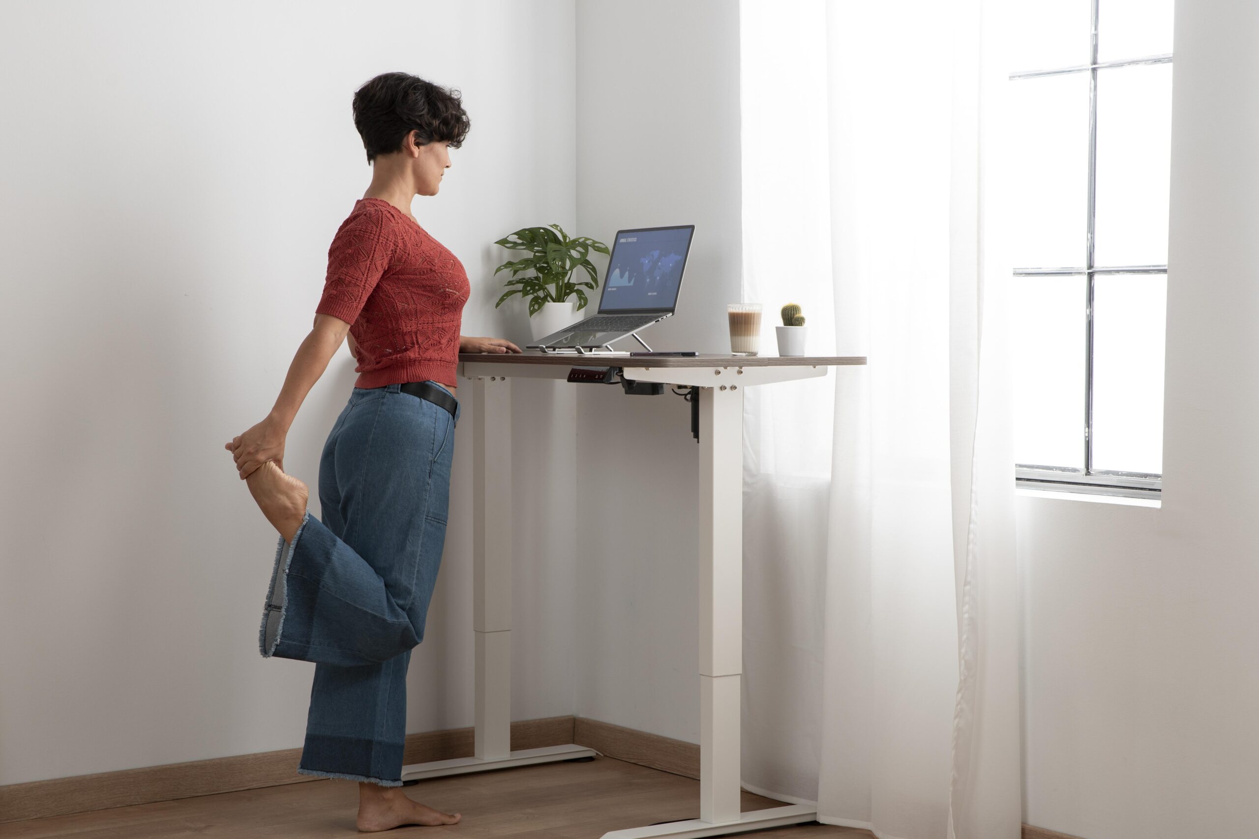 Woman stretching her leg while standing at a desk with dual monitors in a home office.
