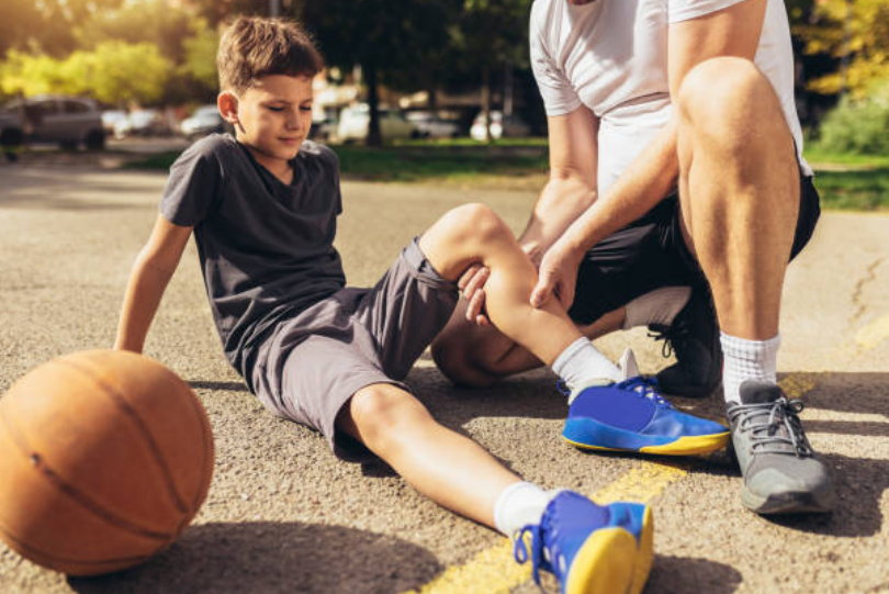 Young boy holding his knee after a sports injury while an adult checks his leg.