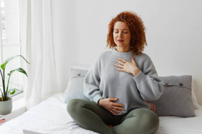Woman sitting on a bed practicing deep breathing for relaxation and stress relief.