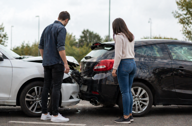Two people standing on the road inspecting damage after a rear-end car accident between two vehicles.