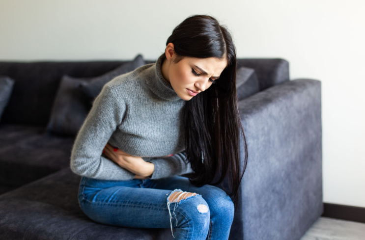 Chiropractic for digestive issues, woman sitting on a couch holding her stomach in discomfort.
