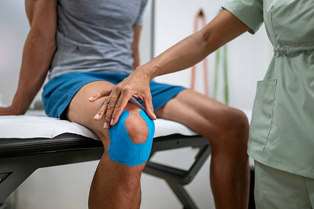Chiropractor applying kinesiology tape to a patient’s knee during treatment.
