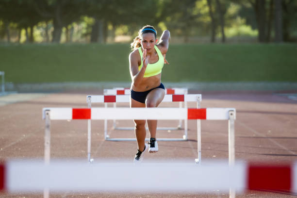 Female athlete sprinting and jumping over hurdles on a track.