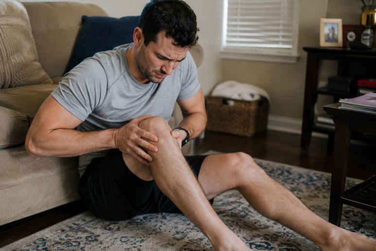 Man sitting on the floor at home holding his knee in pain. 